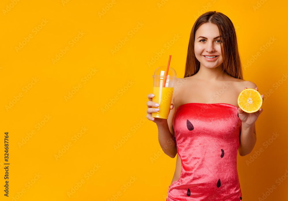 Obraz premium Portrait of a happy smiling woman holding a glass of fruit juice, half an orange on a yellow background