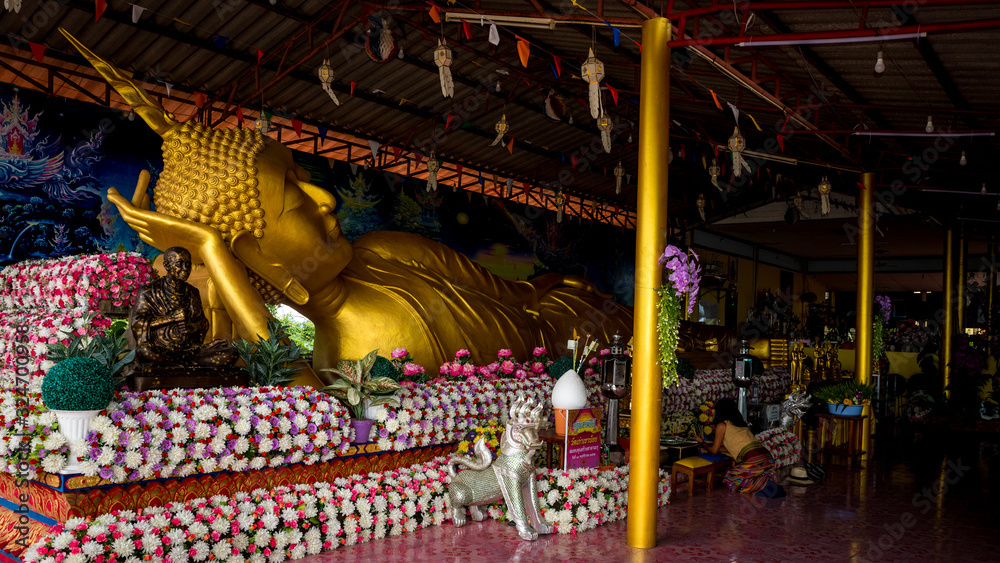 Fototapeta premium Woman praying in wat to reclining Buddha surrounded by flowers
