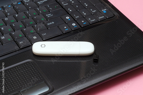 White USB 4G modem is on a laptop, keyboard with Russian and English letters