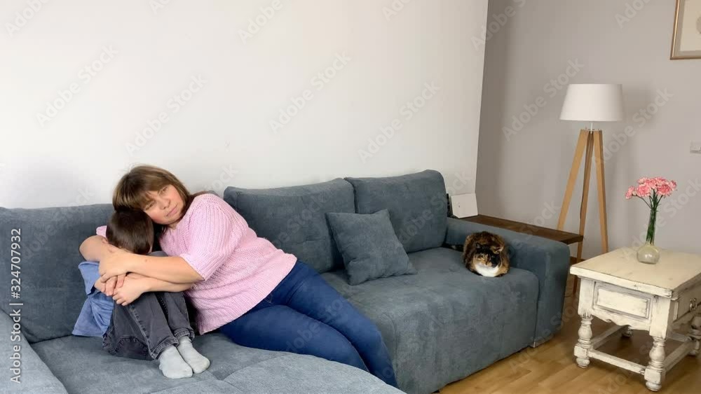 kid, a boy of primary school age in jeans, a blue shirt sits on the couch, covered his face, mom sits nearby, hugs her son, the concept of education kid, a boy of primary school age in jeans, a blue shirt sits on the couch, covered his face, mom sits nearby, hugs her son, the concept of education