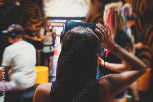 Concept of a girl wearing VR glasses goggles, brunette european girl with virtual reality glasses in the room with other people