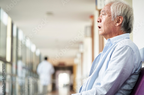 devastated senior asian man sitting in hospital hallway