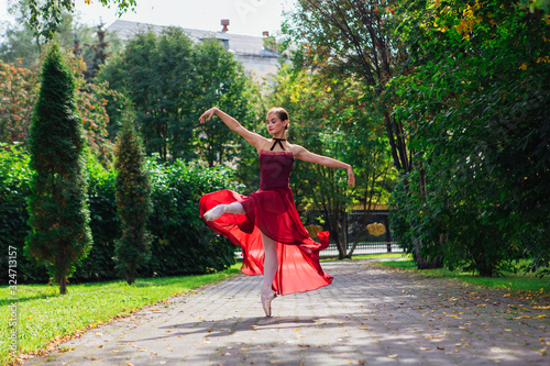 Woman ballerina in red ballet dress dancing in pointe shoes in autumn park.