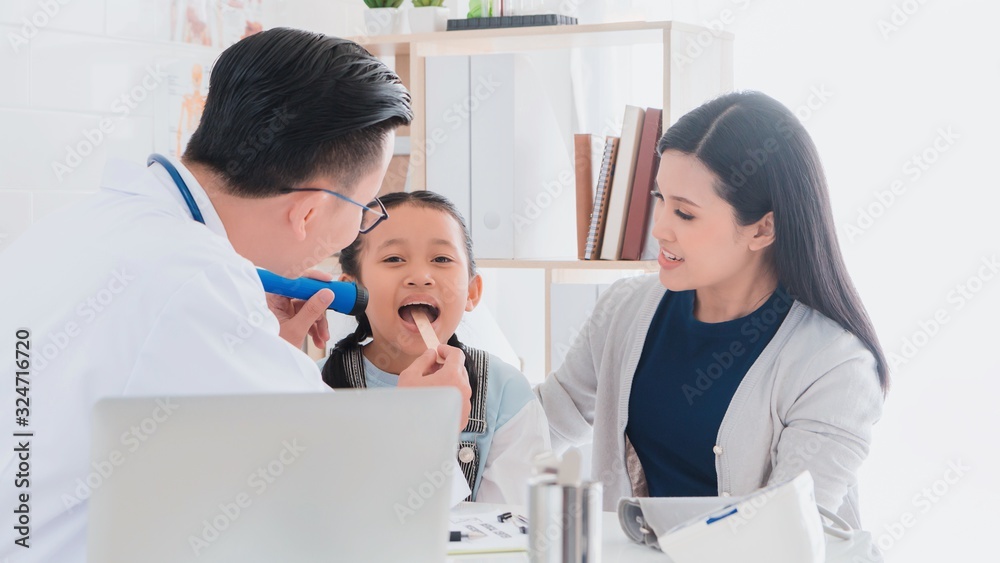 Professional doctor wearing white coat using tongue depressor to examine kid patient with her mother in hospital background.Concept of disease treatment and health care in hospitals. Professional doctor wearing white coat using tongue depressor to examine kid patient with her mother in hospital background.Concept of disease treatment and health care in hospitals.