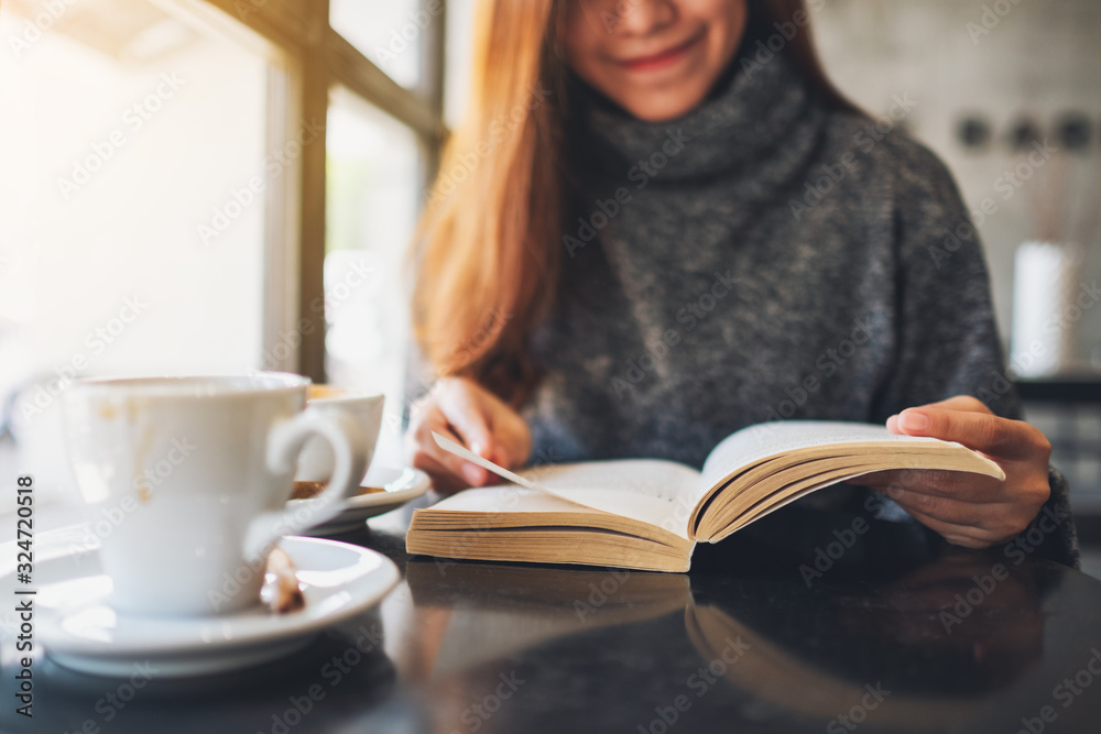 Closeup image of a beautiful woman holding and reading a book with coffee cup on the table Closeup image of a beautiful woman holding and reading a book with coffee cup on the table