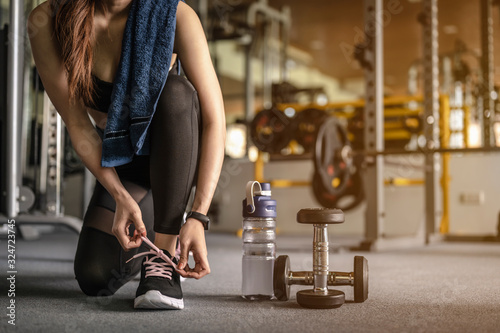 Women are using their hands to tie their shoes, have a dumbbell and a bottle of water. Prepare for exercise in the gym at sunset. fitness, workout, gym exercise, lifestyle and healthy concept. photo