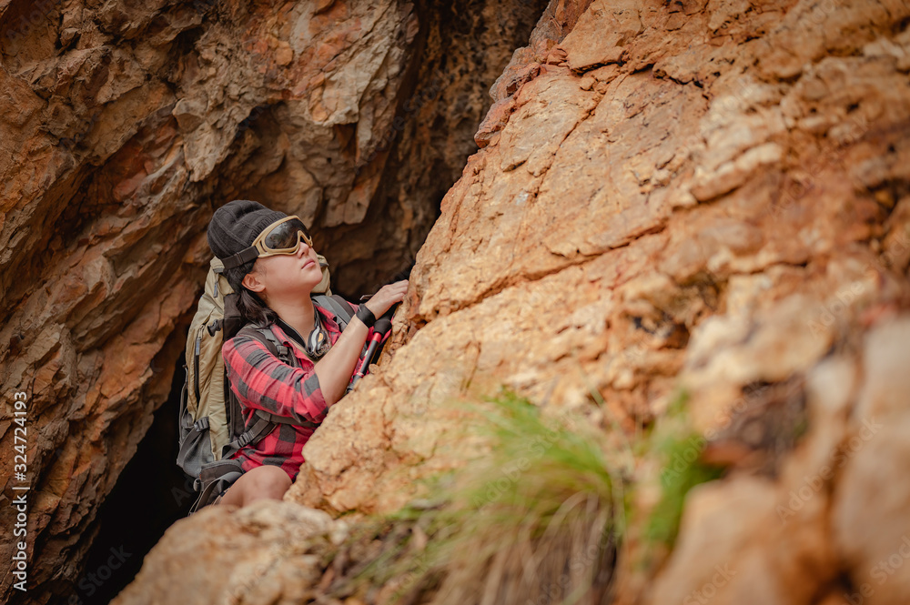 Fototapeta premium Side view of woman hiker climbing on the cliff at cave in sunset. Woman, hiking, hikers, mountain, cave, activity concept.