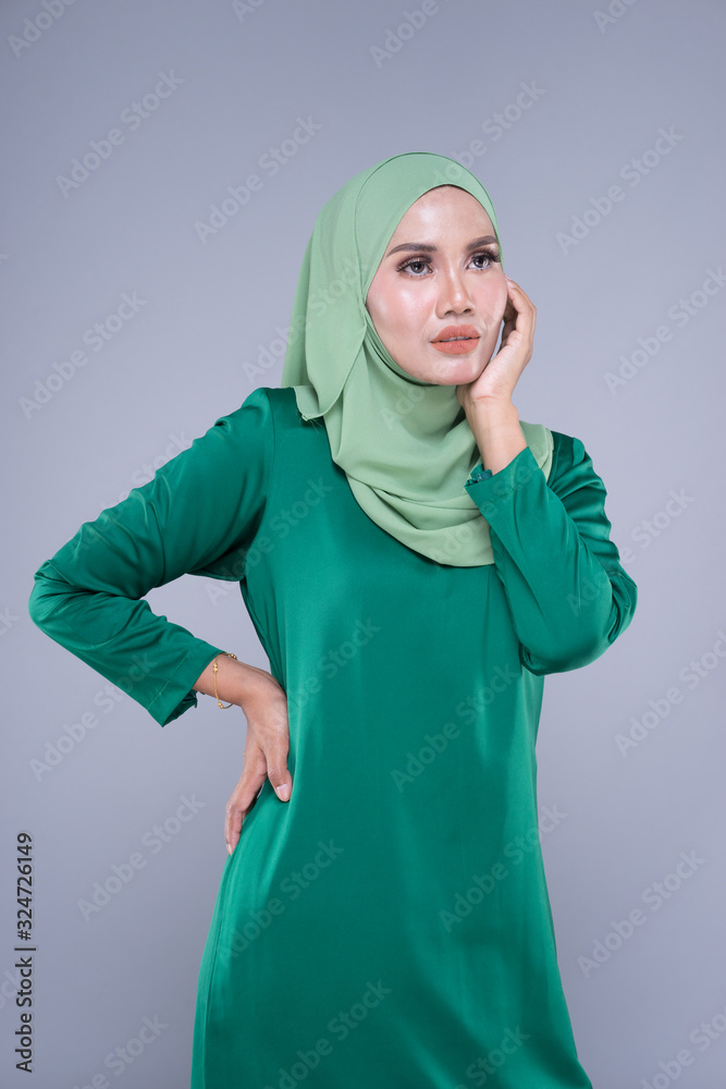 Beautiful female model in modern kurung and hijab, a modern lifestyle apparel for Muslim women isolated on grey background. Beauty and hijab fashion concept. Half length portrait Beautiful female model in modern kurung and hijab, a modern lifestyle apparel for Muslim women isolated on grey background. Beauty and hijab fashion concept. Half length portrait