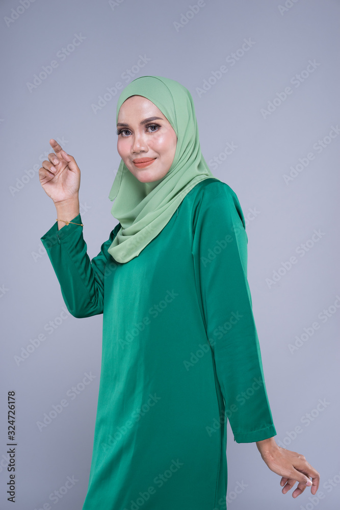 Beautiful female model in modern kurung and hijab, a modern lifestyle apparel for Muslim women isolated on grey background. Beauty and hijab fashion concept. Half length portrait Beautiful female model in modern kurung and hijab, a modern lifestyle apparel for Muslim women isolated on grey background. Beauty and hijab fashion concept. Half length portrait