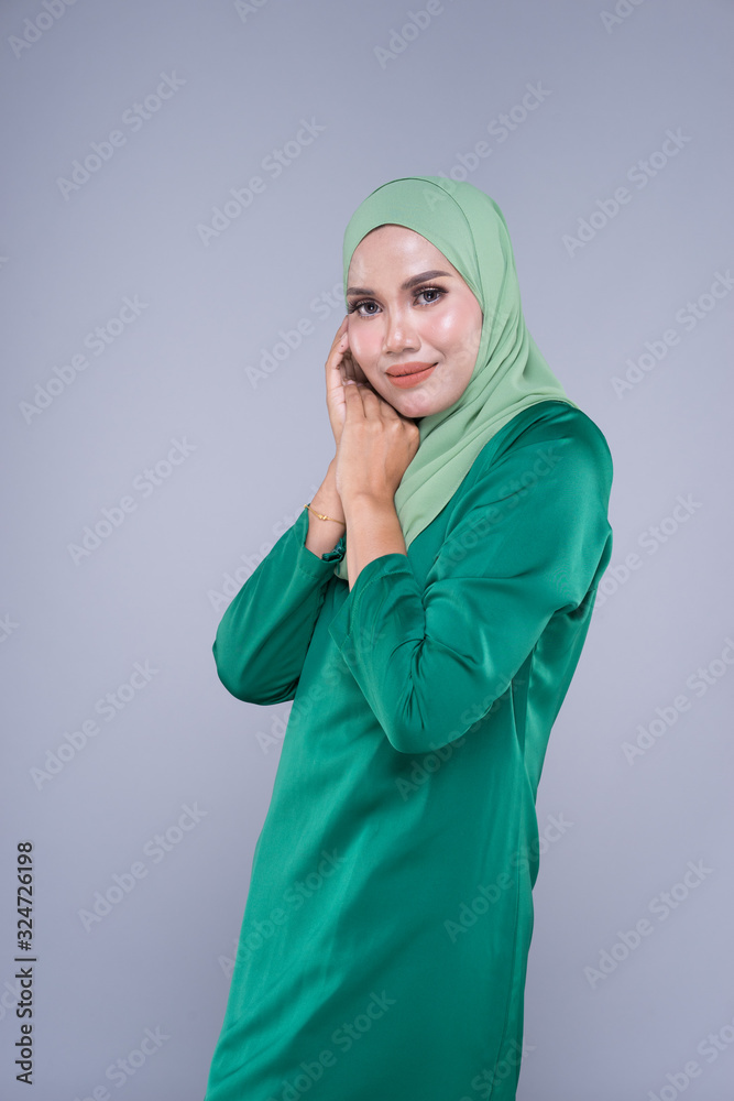 Beautiful female model in modern kurung and hijab, a modern lifestyle apparel for Muslim women isolated on grey background. Beauty and hijab fashion concept. Half length portrait Beautiful female model in modern kurung and hijab, a modern lifestyle apparel for Muslim women isolated on grey background. Beauty and hijab fashion concept. Half length portrait