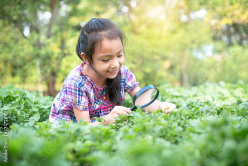 Young girl is looking at tree leaves through magnifier and smiling, education concept