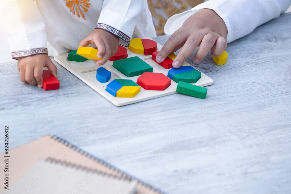 Close up hand of little Muslim boy with tradition suit and mom playing colorful wood blocks in the park, education concept Close up hand of little Muslim boy with tradition suit and mom playing colorful wood blocks in the park, education concept