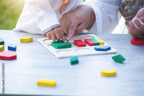 Close up hand of little Muslim boy with tradition suit and mom playing colorful wood blocks in the park, education concept