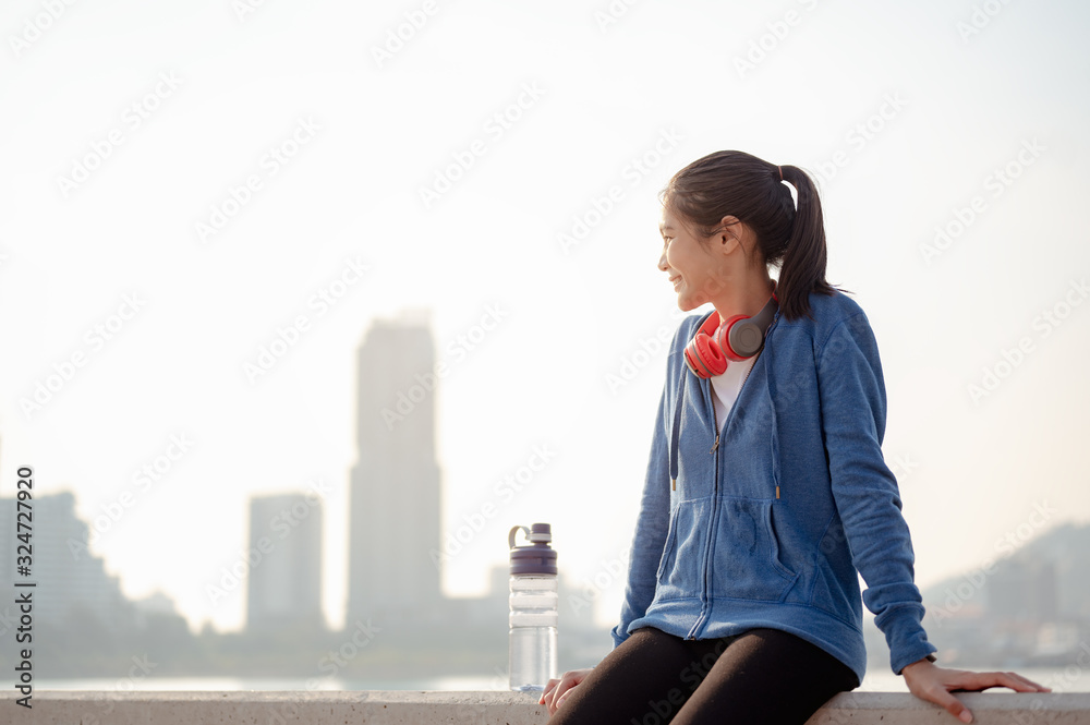 Young woman drink water and stand to rest after jogging a morning workout in the city. A city that lives healthy in the capital. Exercise, fitness, jogging, running, lifestyle, healthy concept.
