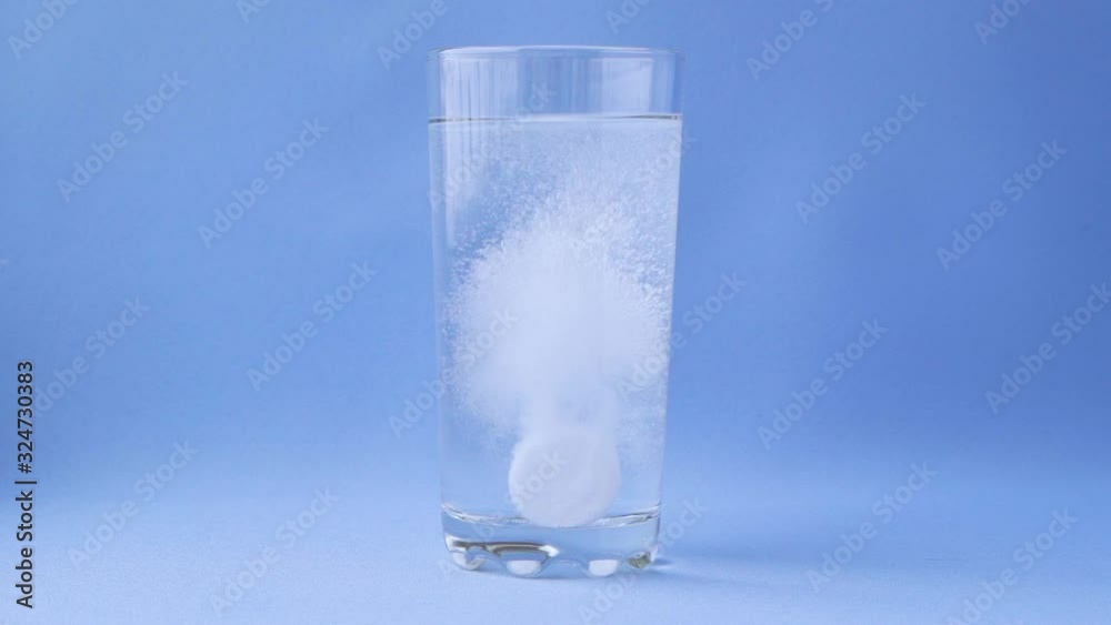 Aspirin dissolves in a glass of water on a blue background close-up, effervescent aspirin. Slow motion.