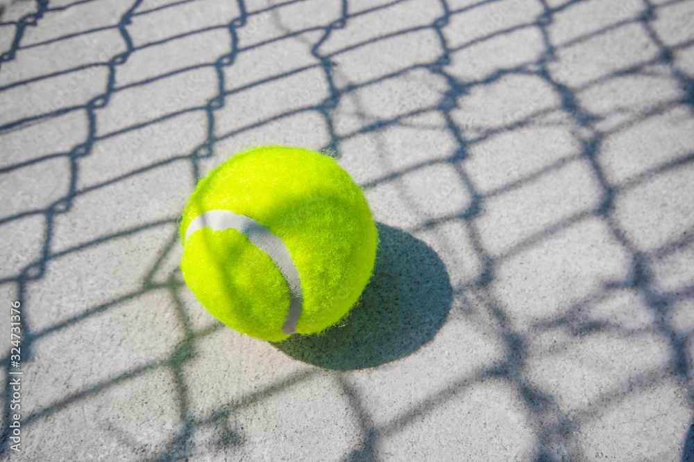 The tennis ball is placed on the concrete floor. There is a shadow of the net.