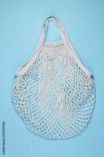 White cotton mesh bag on blue paper background. Reusable shopping bag on color background. Ecological, Zero waste concept. Top view, flat lay, copy space