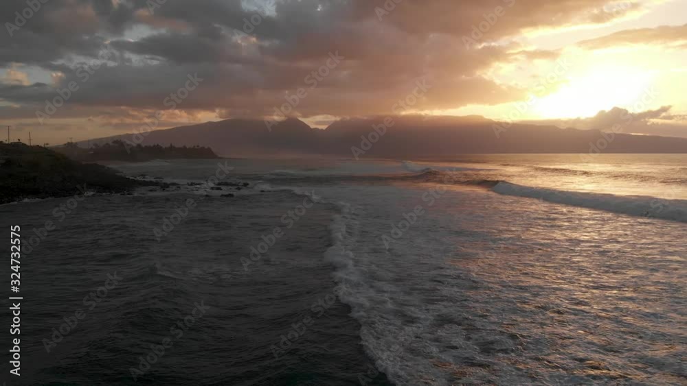 A drone flies captures the waves of Maui, Hawaii's north shore near Ho'Okipa as the golden sun sets over the west mountains. A drone flies captures the waves of Maui, Hawaii's north shore near Ho'Okipa as the golden sun sets over the west mountains.