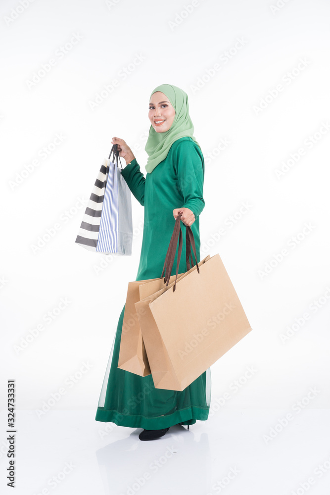 A beautiful Asian female model in a modern kurung carrying shopping bags isolated on white background. Eidul fitri festive preparation shopping concept. Full length portrait. A beautiful Asian female model in a modern kurung carrying shopping bags isolated on white background. Eidul fitri festive preparation shopping concept. Full length portrait.