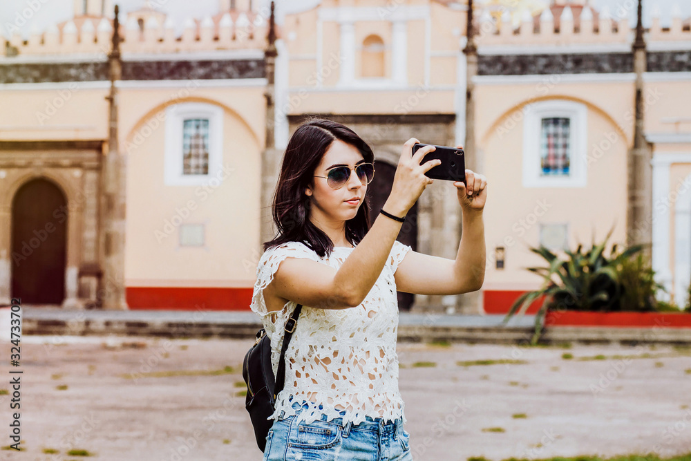 Latin woman in summer sun glasses and holding a smart phone taking a photo in Mexico City, tourist Mexican girl