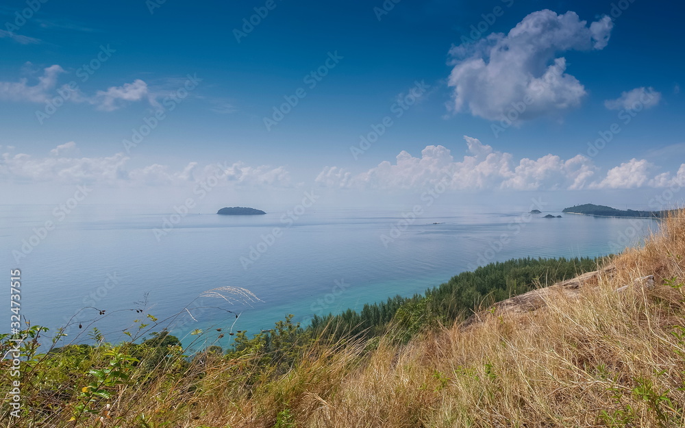 Mountain view of pine forest seaside with Lipe island in blue-green sea and blue sky background, taken from Chado Cliff view point, Adang island, Tarutao Marine National Park, Satun, southern Thailand