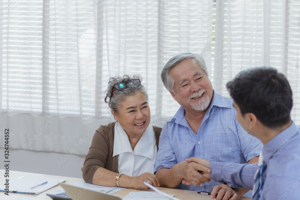 Fototapeta premium Happy retired Asian senior eldery couple hands shaking business deal and agreement with personal financial advisor or real estate agent. Retirement investment planning with professional counseling.