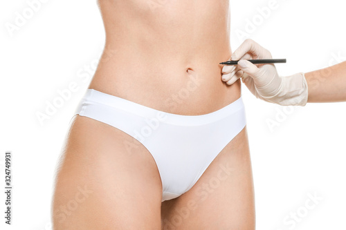 Plastic surgeon applying marks on female body against white background