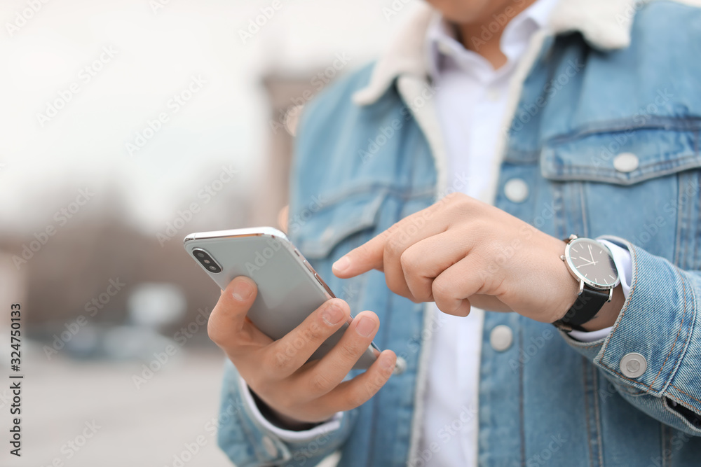 Young man with mobile phone outdoors, closeup