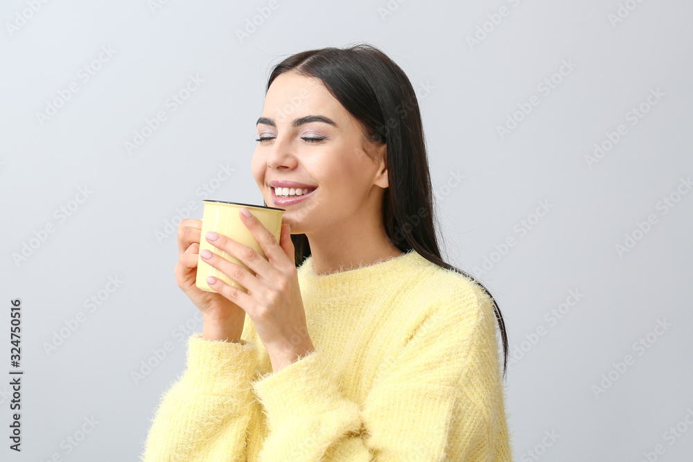 Beautiful young woman in warm sweater drinking tea on light background Beautiful young woman in warm sweater drinking tea on light background