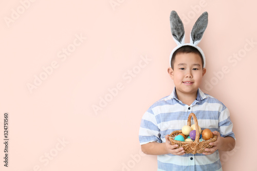 Little Asian boy with Easter eggs and bunny ears on color background