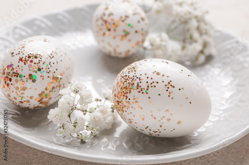 Plate with beautiful Easter eggs and flowers on light background, closeup
