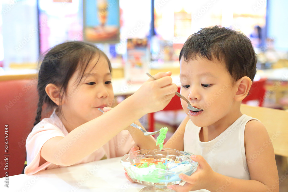 Asian sister and her little brother eating icecream together. Child girl feeding ice cream for baby boy in cafe. Asian sister and her little brother eating icecream together. Child girl feeding ice cream for baby boy in cafe.