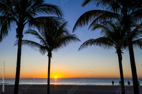 Sunrise or sunset in the Caribbean with blue sky and silhouette palm trees and people on the seashore enjoying the stunning view.