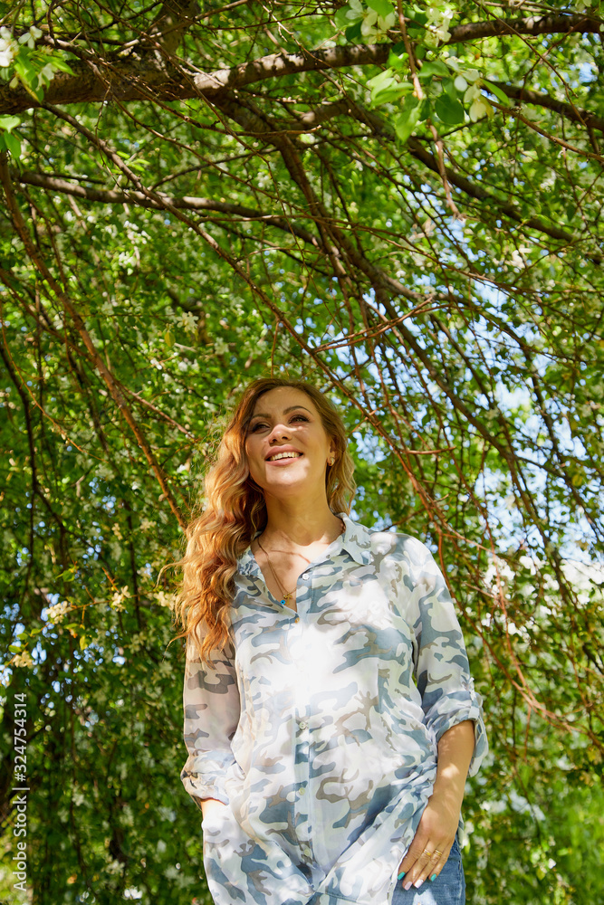 Portrait of a beautiful blonde girl with green eyes and blossoming apple tree with white flower in the park in a spring time Portrait of a beautiful blonde girl with green eyes and blossoming apple tree with white flower in the park in a spring time