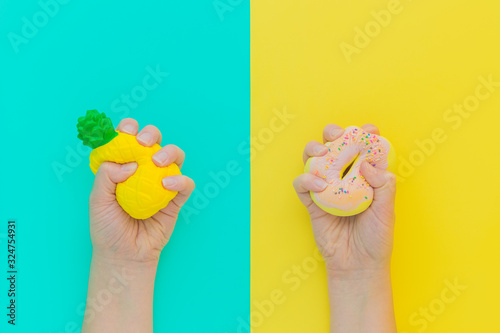 Flat lay antistress squish toys yellow pineapple,pink donut with sprinkles in hands.Bright blue background.Compressing,soft,squeezable items to relieve stress,problem,anxieties,worries.Summer concept photo