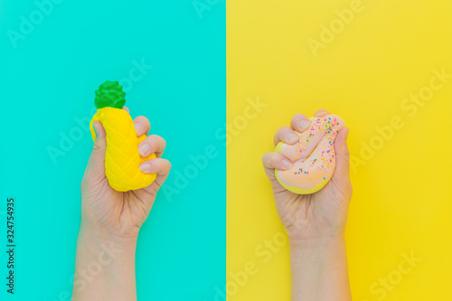Flat lay antistress squish toys yellow pineapple,pink donut with sprinkles in hands.Bright blue background.Compressing,soft,squeezable items to relieve stress,problem,anxieties,worries.Summer concept photo