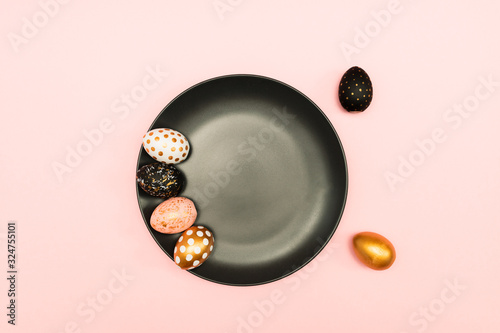 Top view of pink, white and golden decorated eeaster eggs on black plate on pink background. Trendy holiday backdrop. photo