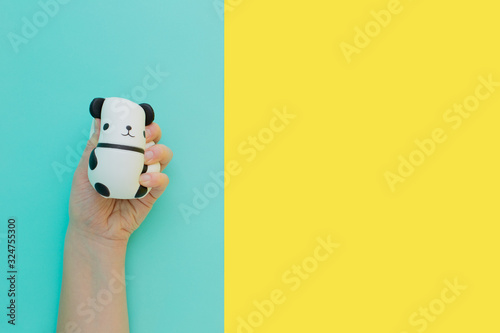 Flat lay antistress toy squish black white big panda squeezed in hand.Bright yellow blue background.Compressing, soft, squeezable items to relieve stress, problems, anxieties, worries.Summer concept photo