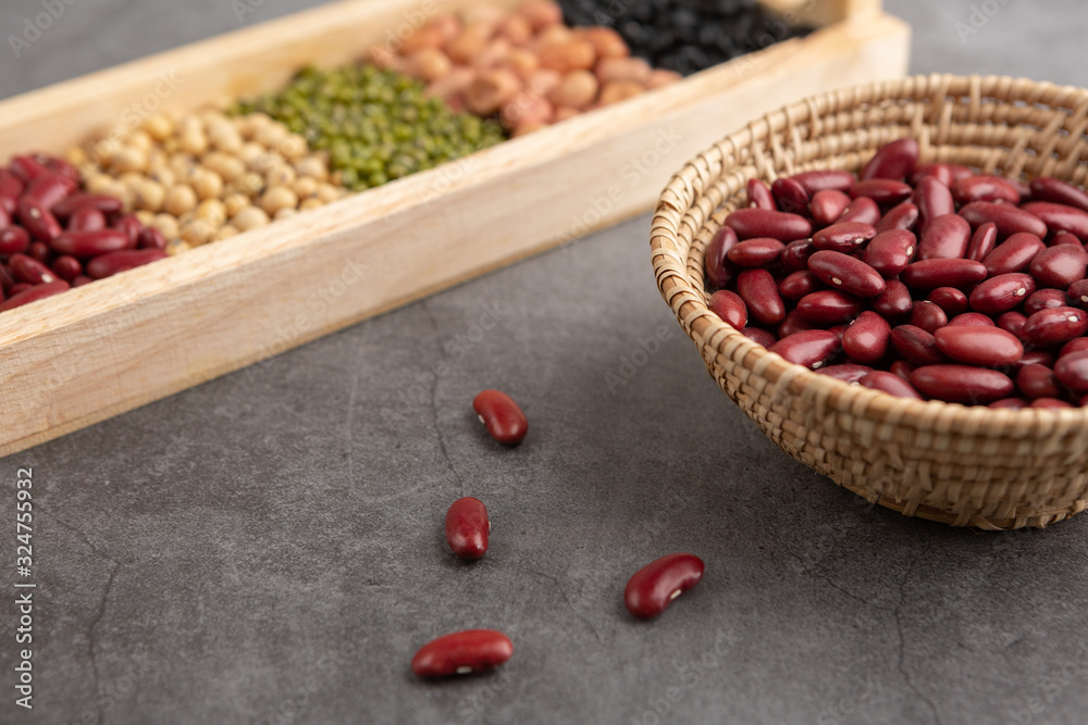 Red beans and grains in the wooden basket and in the wooden tray placed on the black cement floor. High angle view. Red beans and grains in the wooden basket and in the wooden tray placed on the black cement floor. High angle view.