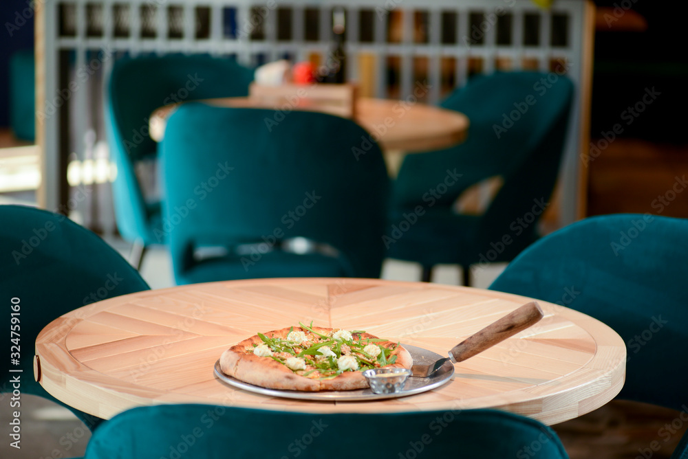 Delicious Italian large pizza served on a light wooden table in a restaurant. Restaurant food photography