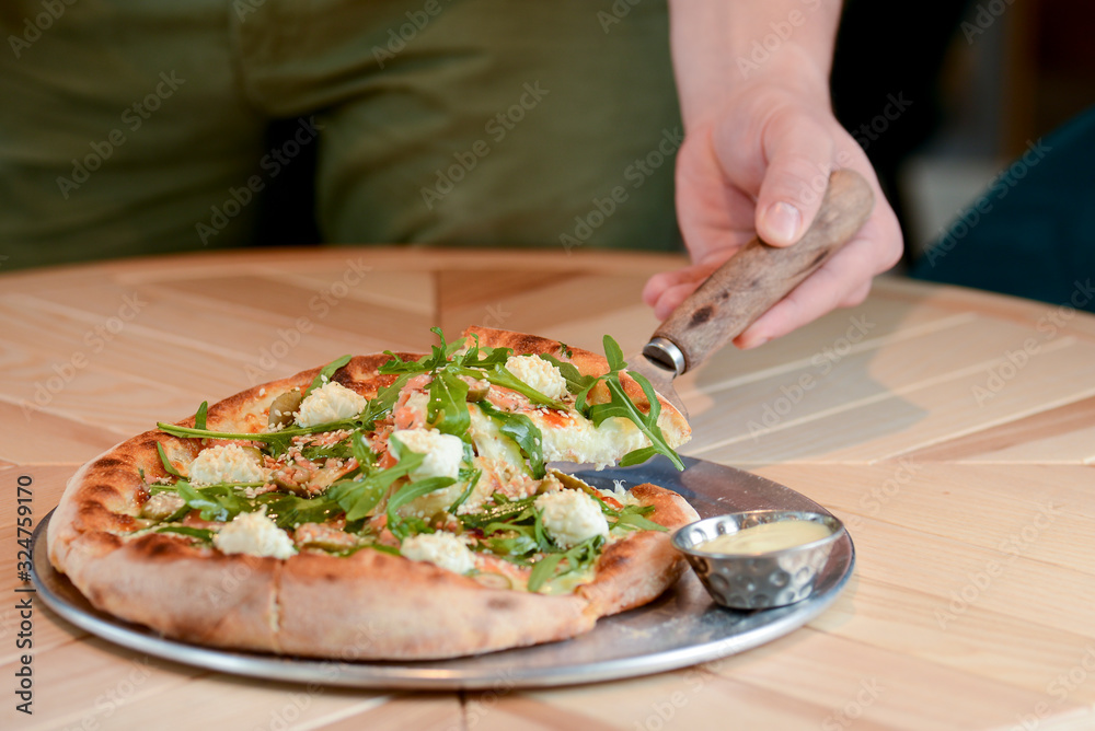 Delicious Italian large pizza served on a light wooden table in a restaurant. Restaurant food photography