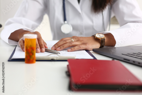 Female black medicine doctor hand hold jar of pills and write prescription to patient at worktable. Panacea and life save, prescribing treatment legal drug store concept. Empty form ready to be used