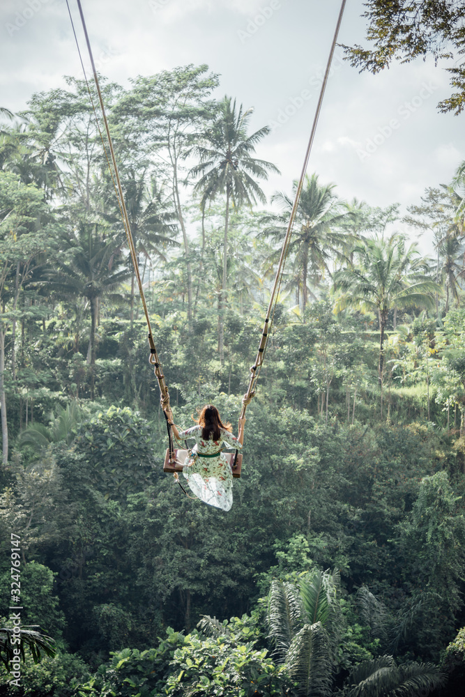 A woman in light green dress enjoy her holiday activity of sitting on giant swing in Bali, Indonesia.