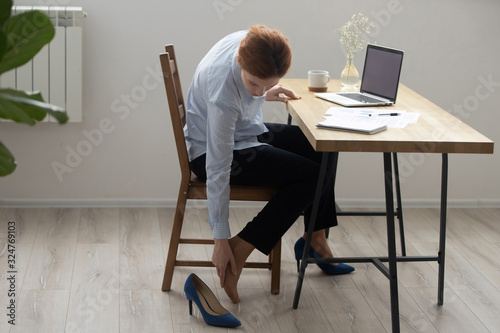 Businesswoman massaging foot, feeling discomfort after shoes with heels photo