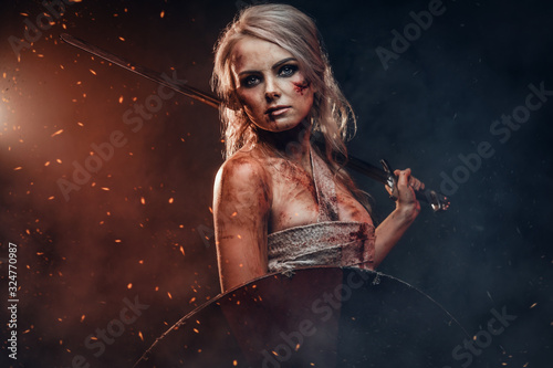 Fantasy woman warrior wearing rag cloth stained with blood and mud, holding sword and shield. Studio photo on a dark background. Cosplayer as Ciri from The Witcher