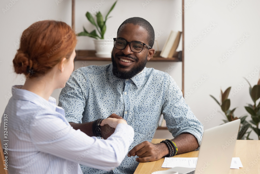 Obraz premium Businesswoman shaking hand of African American colleague at workplace