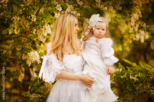 mom and daughter in white vintage dresses walk in the spring garden