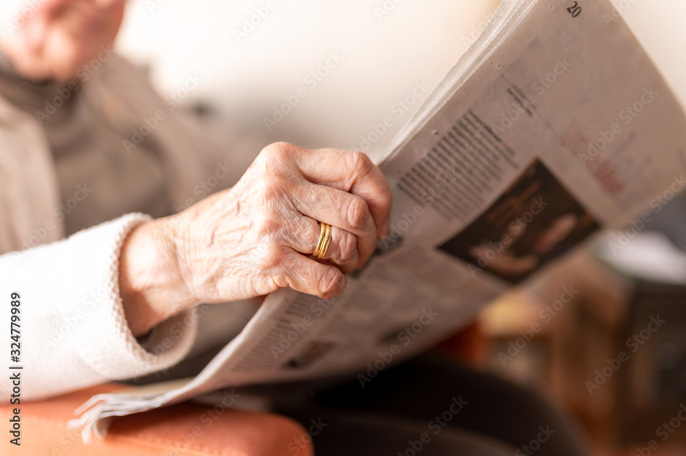 Obraz premium Old woman reading a newspaper. Her wrinkled hand with her wedding ring and that of her deceased husband is close up.