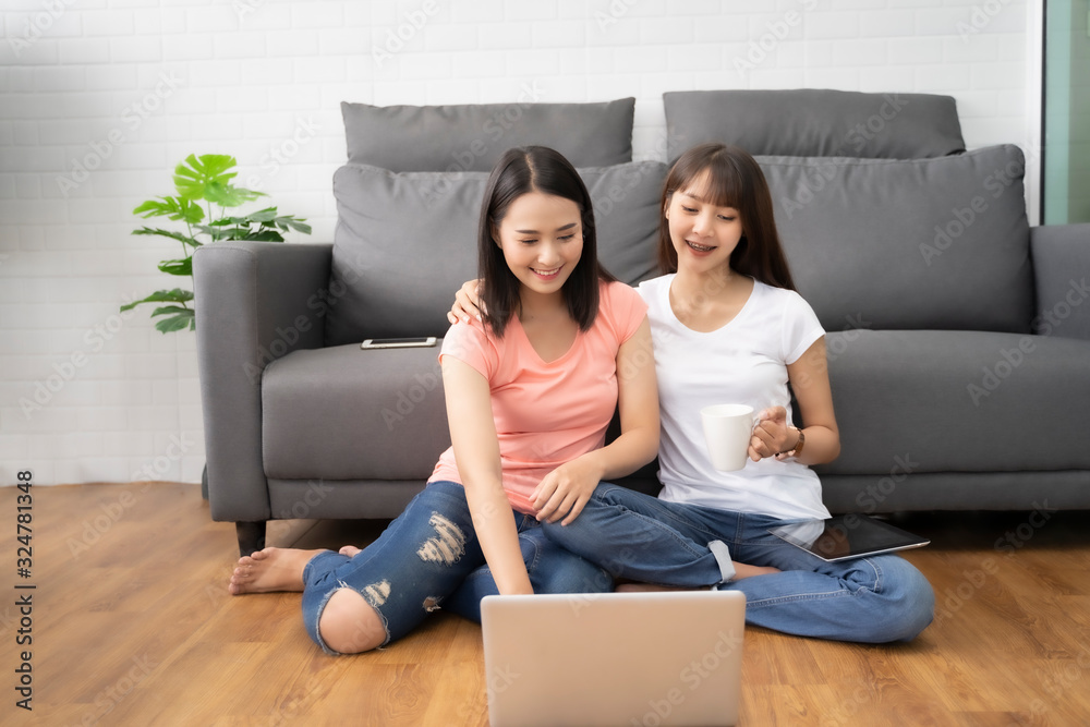 Asian women couple two LGBT lesbian happy couple sitting near a sofa using a laptop tablets, phone for shopping online in the living room at home. LGBT lesbian couple community together concept. Asian women couple two LGBT lesbian happy couple sitting near a sofa using a laptop tablets, phone for shopping online in the living room at home. LGBT lesbian couple community together concept.