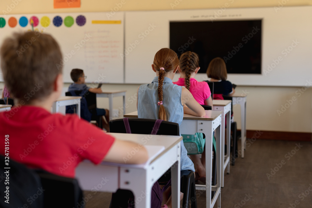 Obraz premium Grupa uczniów siedzących przy ławkach w klasie szkoły podstawowej